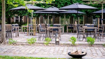 An outdoor patio area with multiple tables and chairs under umbrellas, surrounded by brick walls and greenery.