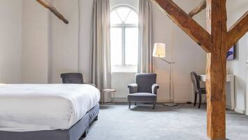 A bedroom with a bed, two chairs, a desk, and a window with curtains.