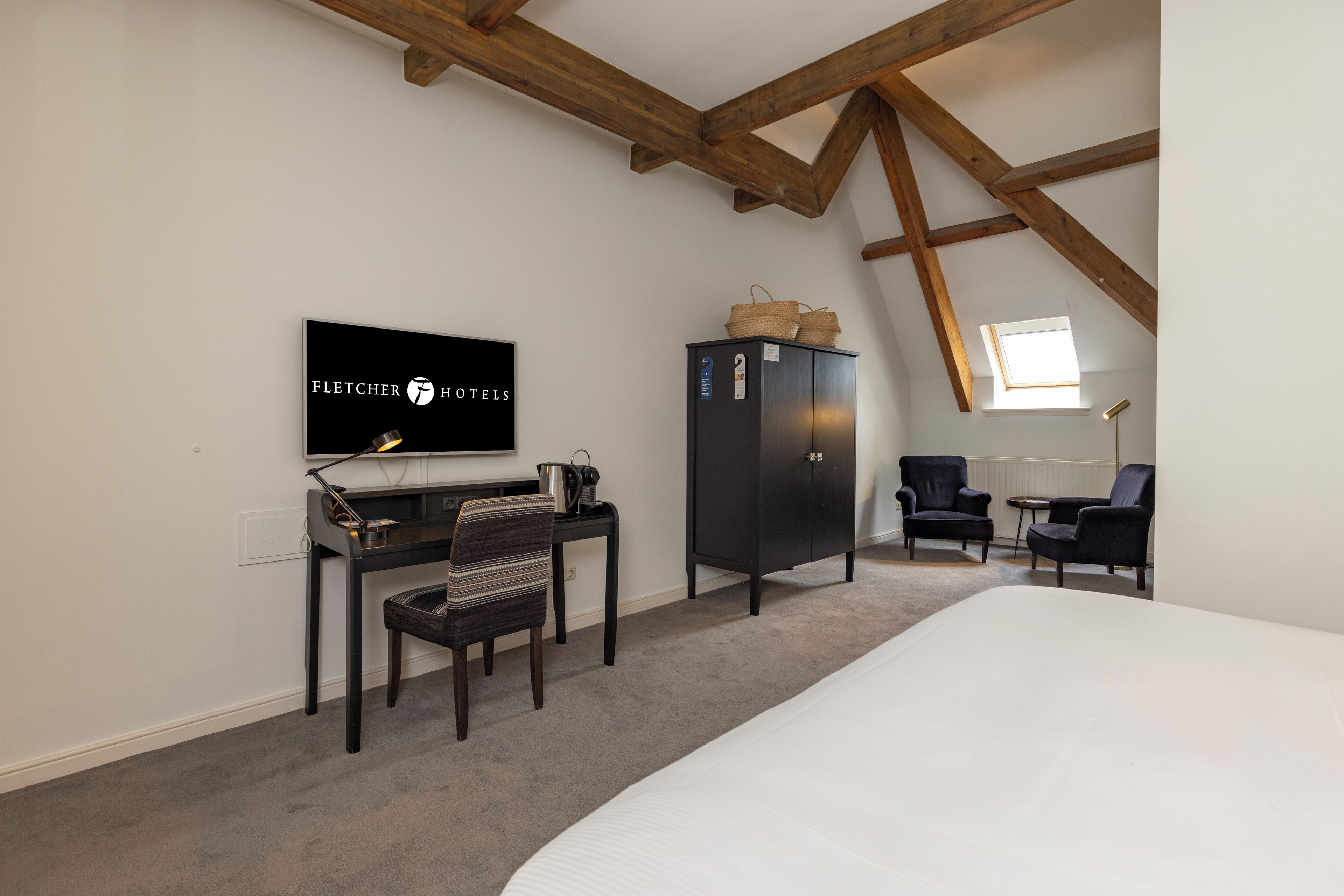 Ein Hotelzimmer mit Bett, Schreibtisch mit Stuhl, Fernseher, Kleiderschrank und Fenster.