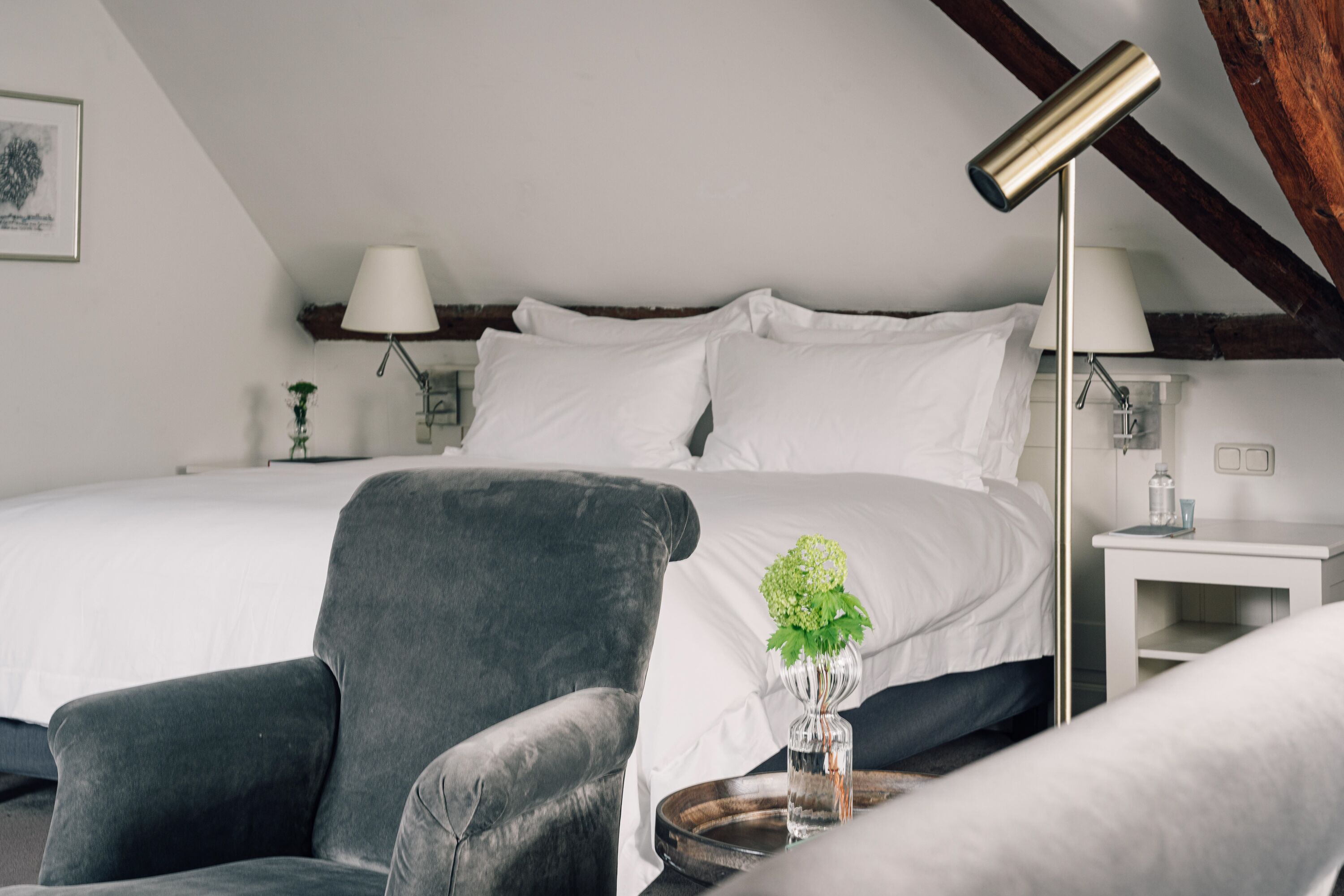 A neatly arranged bedroom with a large bed, a bedside table with a lamp, and a chair.