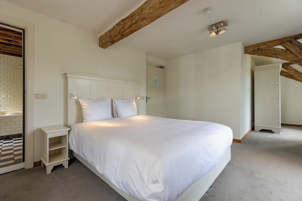 A bedroom with a large bed, a nightstand, and a wooden ceiling beam.