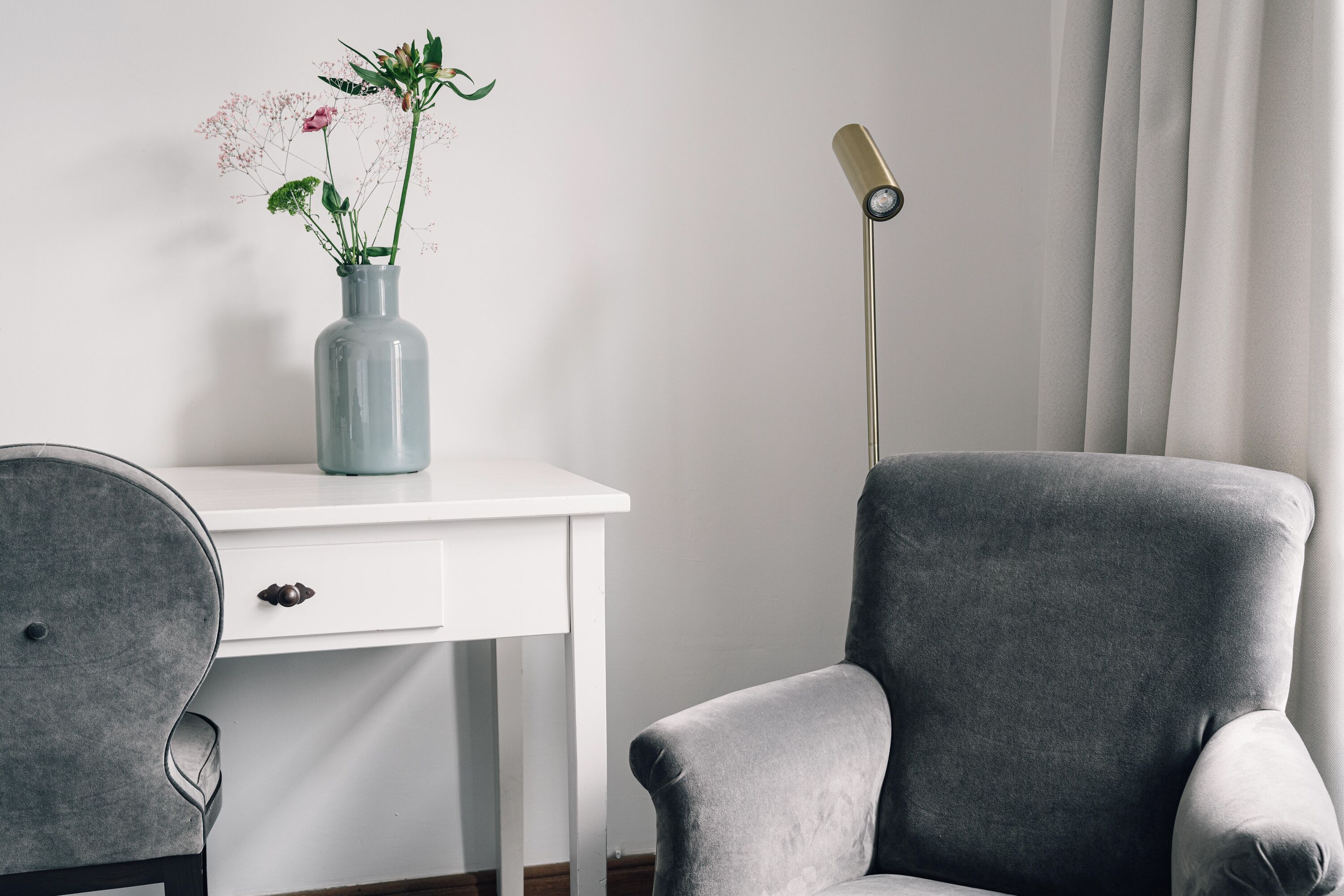A modern room with a grey armchair, a white desk, and a vase with flowers.