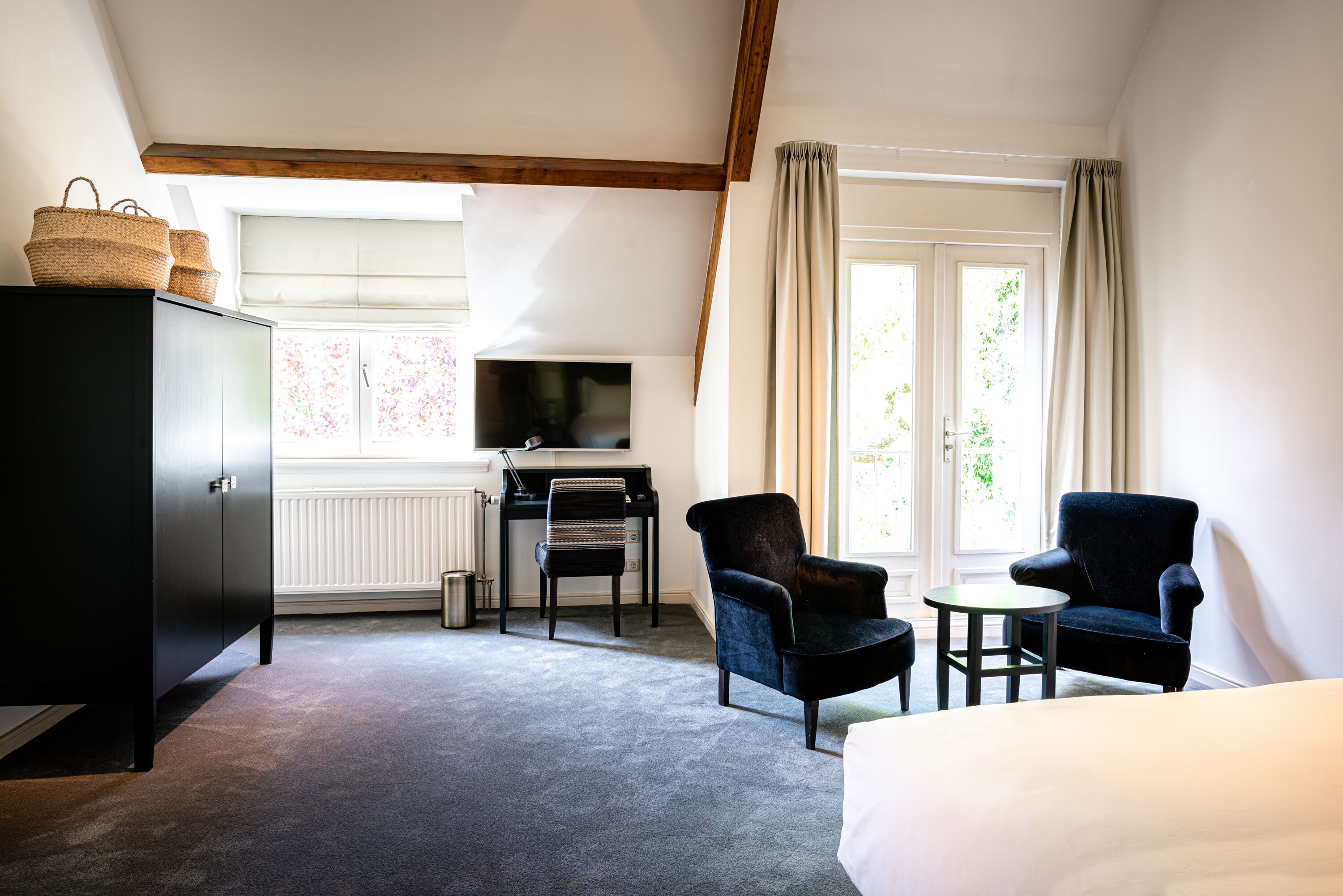 Een hotelkamer met een bed, een bureau met stoel, een televisie en een kledingkast.
