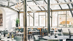 Un restaurante con techo alto y ventanas amplias, con mesas y sillas dispuestas para comer.