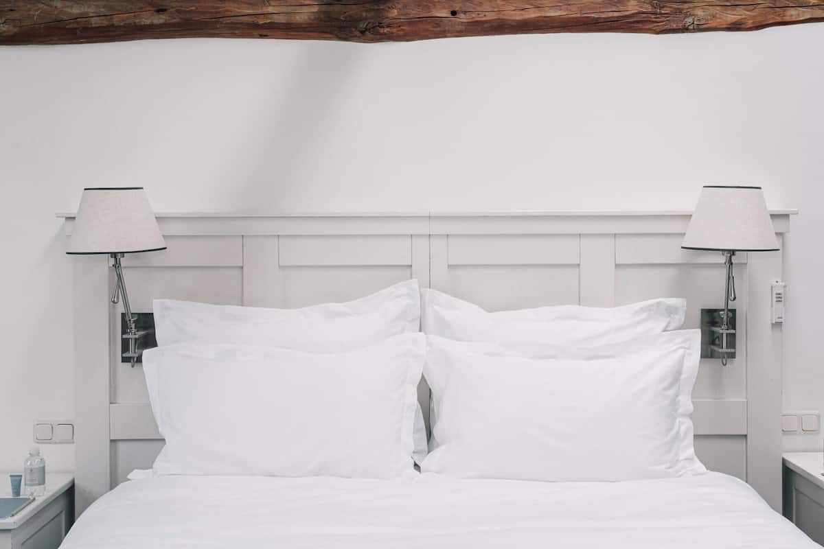 A white bed with two pillows, a wooden ceiling beam, and two bedside lamps.