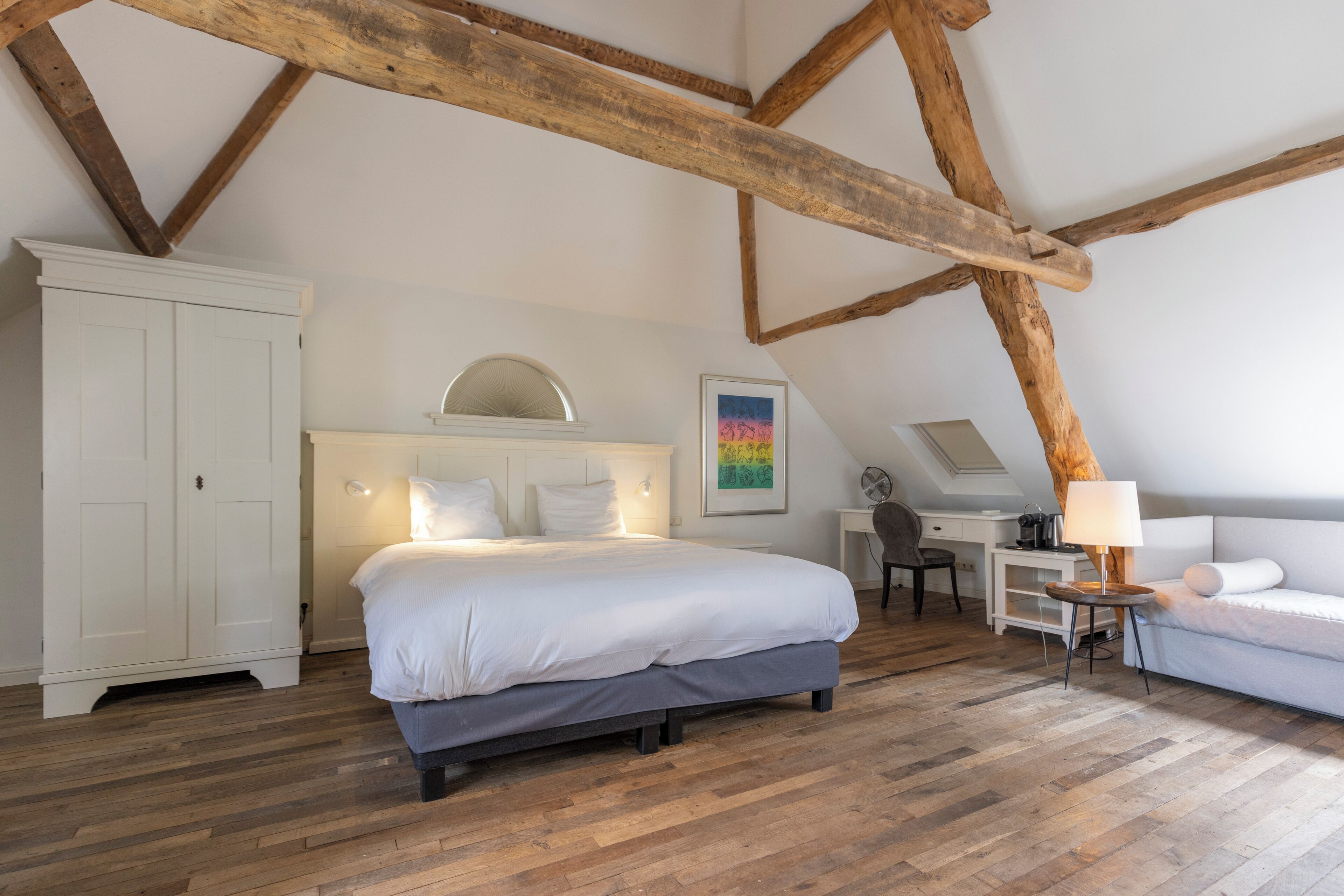 Ein Schlafzimmer mit einem großen Bett, einem Schreibtisch und einem Stuhl. Es gibt einen Kleiderschrank und eine Lampe auf einem Nachttisch.