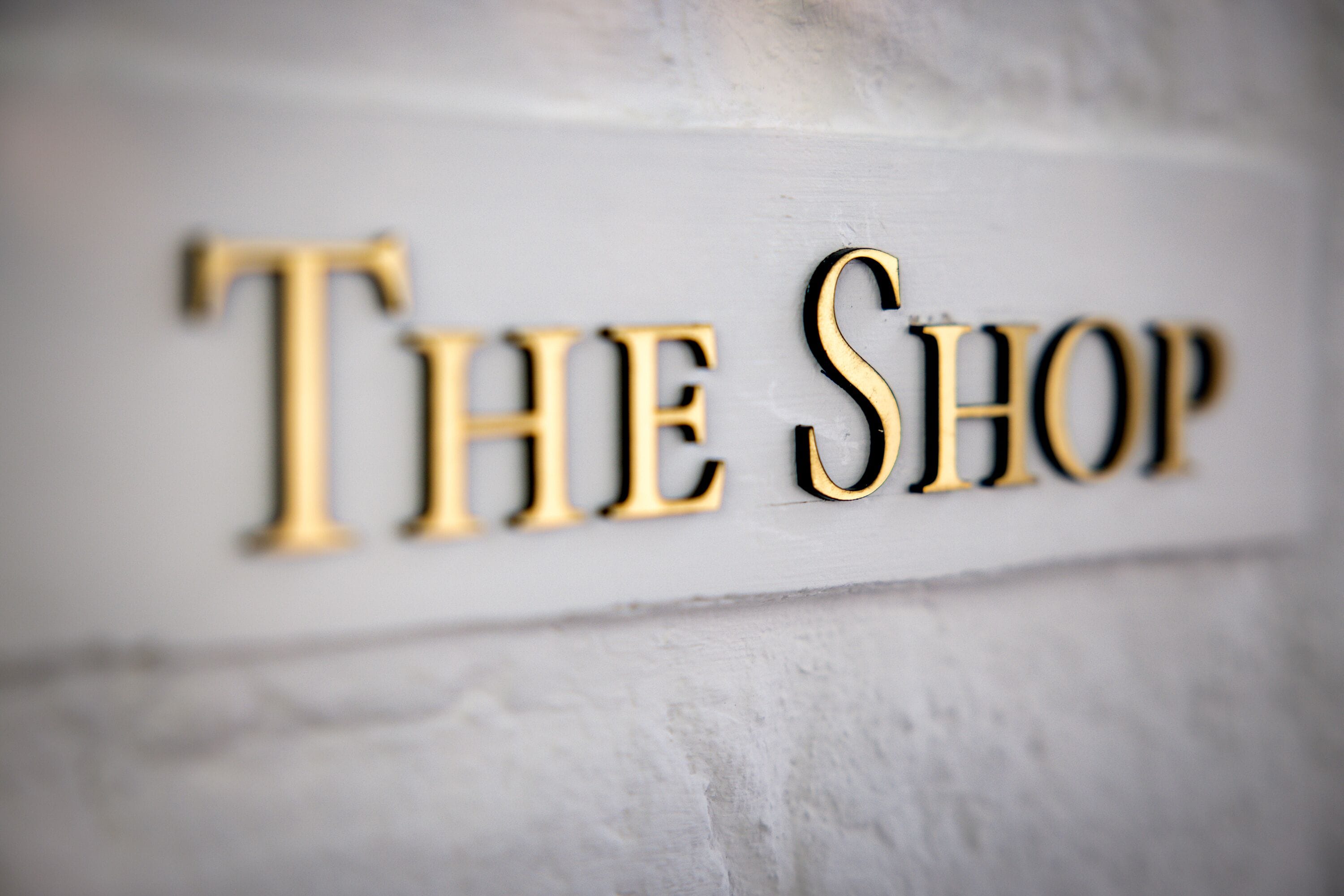 A sign with the words "THE SHOP" in a serif font, mounted on a textured wall.