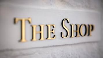 A sign with the words "THE SHOP" in a serif font, mounted on a textured wall.