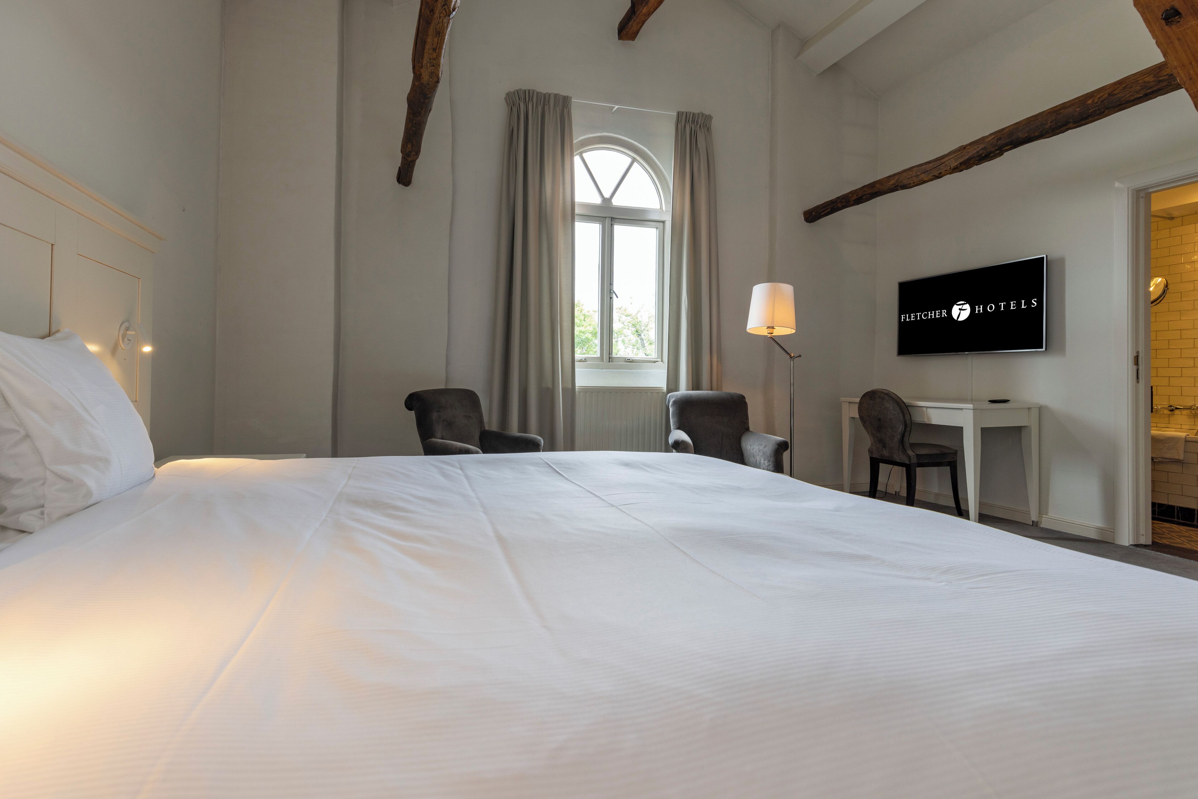 A hotel room with a large bed, two armchairs, a desk, and a television.