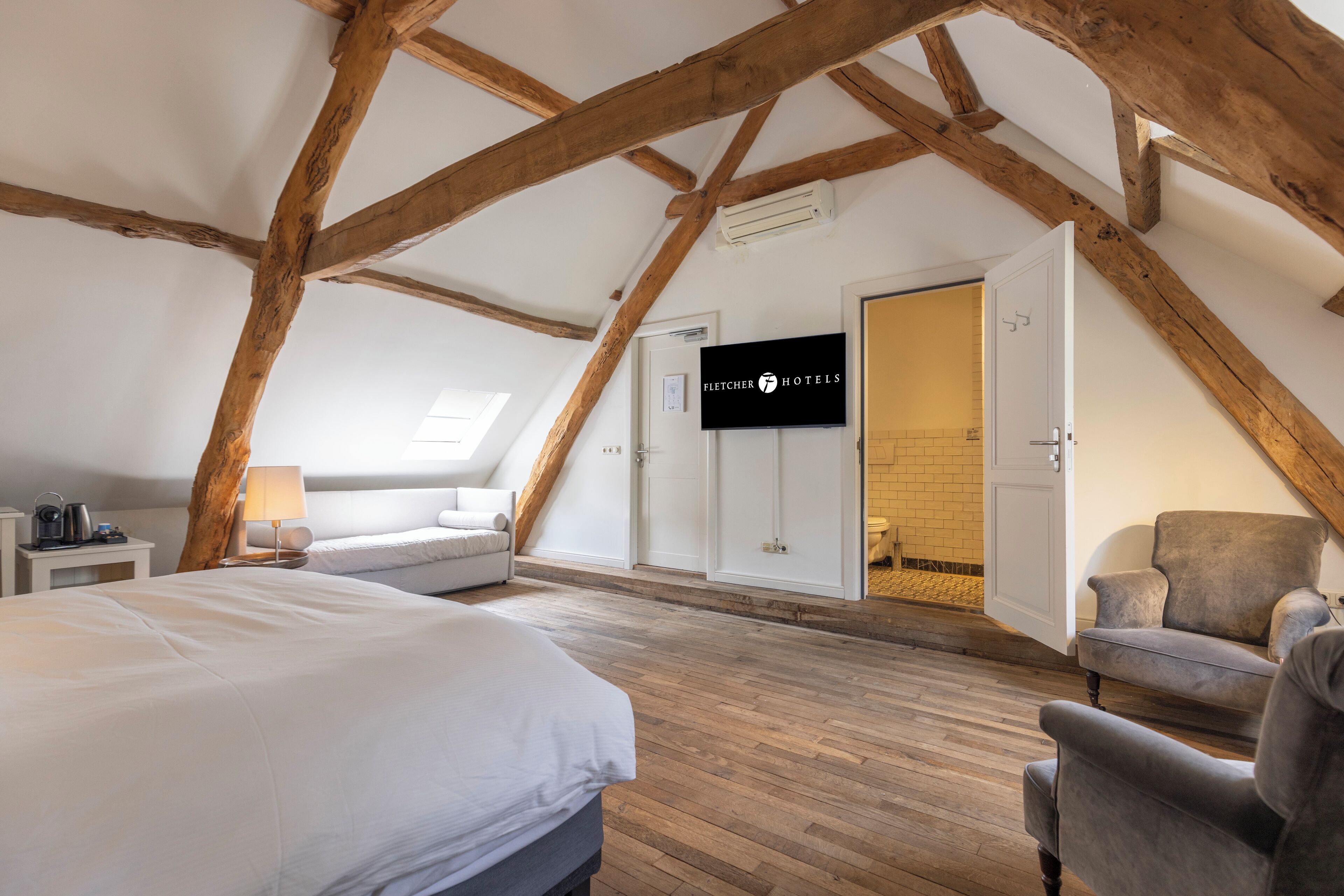 A room with a bed, a chair, a TV, and a door leading to a bathroom.