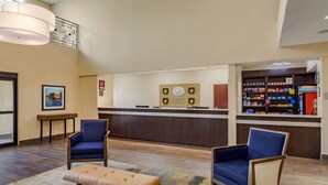 A hotel lobby with a reception desk, two blue armchairs, a bench, and a wall-mounted clock. - Comfort Suites Baytown I - 10 (Baytown)