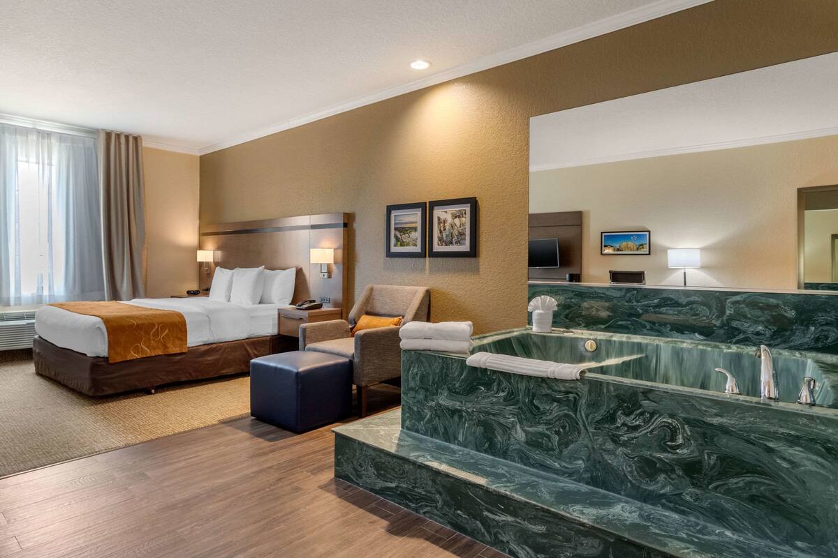 A hotel room with a bed, a seating area, a massage chair, a bathtub, and a TV.