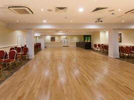 Una amplia sala de conferencias con piso de madera, filas de sillas rojas, una zona de bar y un pilar blanco.