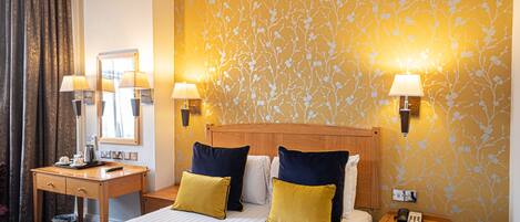 A hotel room with a large bed, two bedside tables, a wooden headboard, and a floral wallpaper.