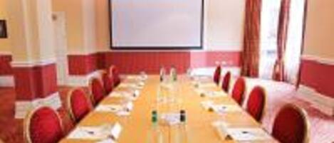 Une salle de conférence avec une longue table, des chaises rouges, un écran de projection et un tableau blanc.