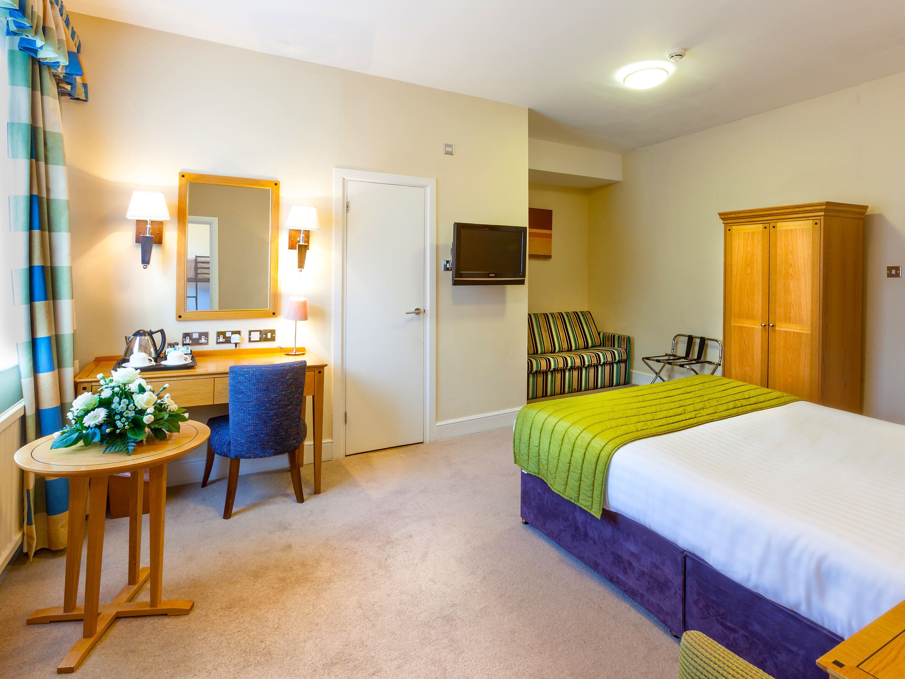 A hotel room with a bed, a desk, a chair, a TV, and a wardrobe.