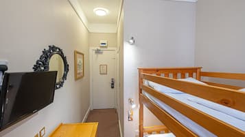 A room with a bunk bed, a flat-screen TV mounted on the wall, a wooden table, and a door with a light switch and a small sign above it.