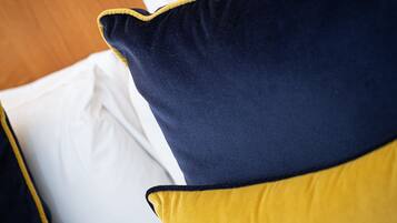 Primer plano de una cama con sábana blanca y dos almohadas, una azul oscuro y otra amarilla.
