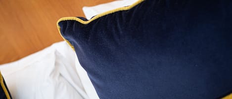 A close-up of a bed with a white sheet and two pillows, one dark blue and one yellow.