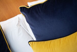 Primer plano de una cama con sábana blanca y dos almohadas, una azul oscuro y otra amarilla.
