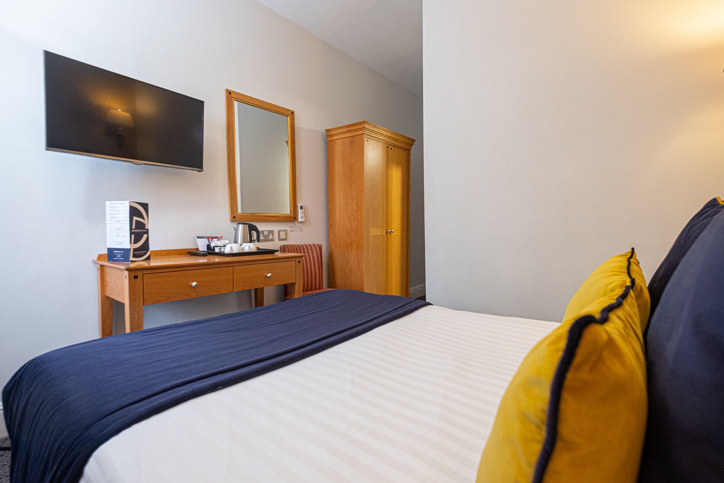 A hotel room with a bed, a wooden dresser, a mirror, and a flat-screen TV mounted on the wall.
