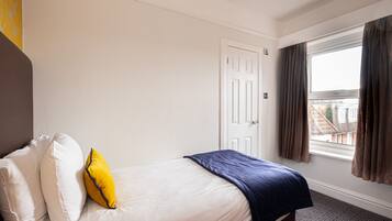 A hotel room with a bed, white walls, a door, and a window with curtains.