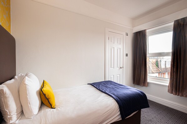 A hotel room with a bed, white walls, a door, and a window with curtains. - The Durley Dean Hotel (Bournemouth)