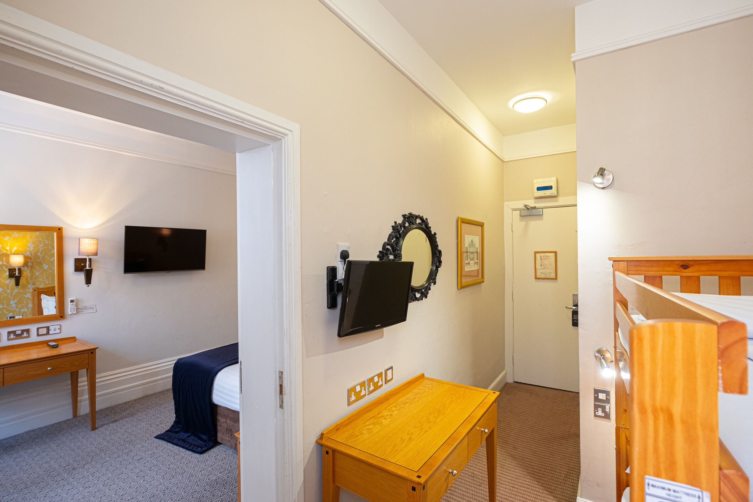 Ein Hotelzimmer mit Bett, Nachttisch, an der Wand montiertem Fernseher und einem kleinen Holztisch.