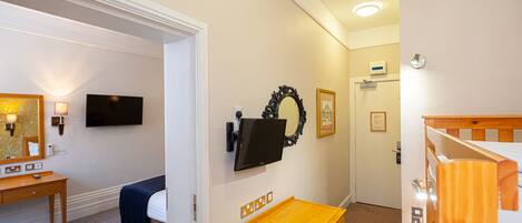 A hotel room with a bed, bedside table, wall-mounted TV, and a small wooden table.