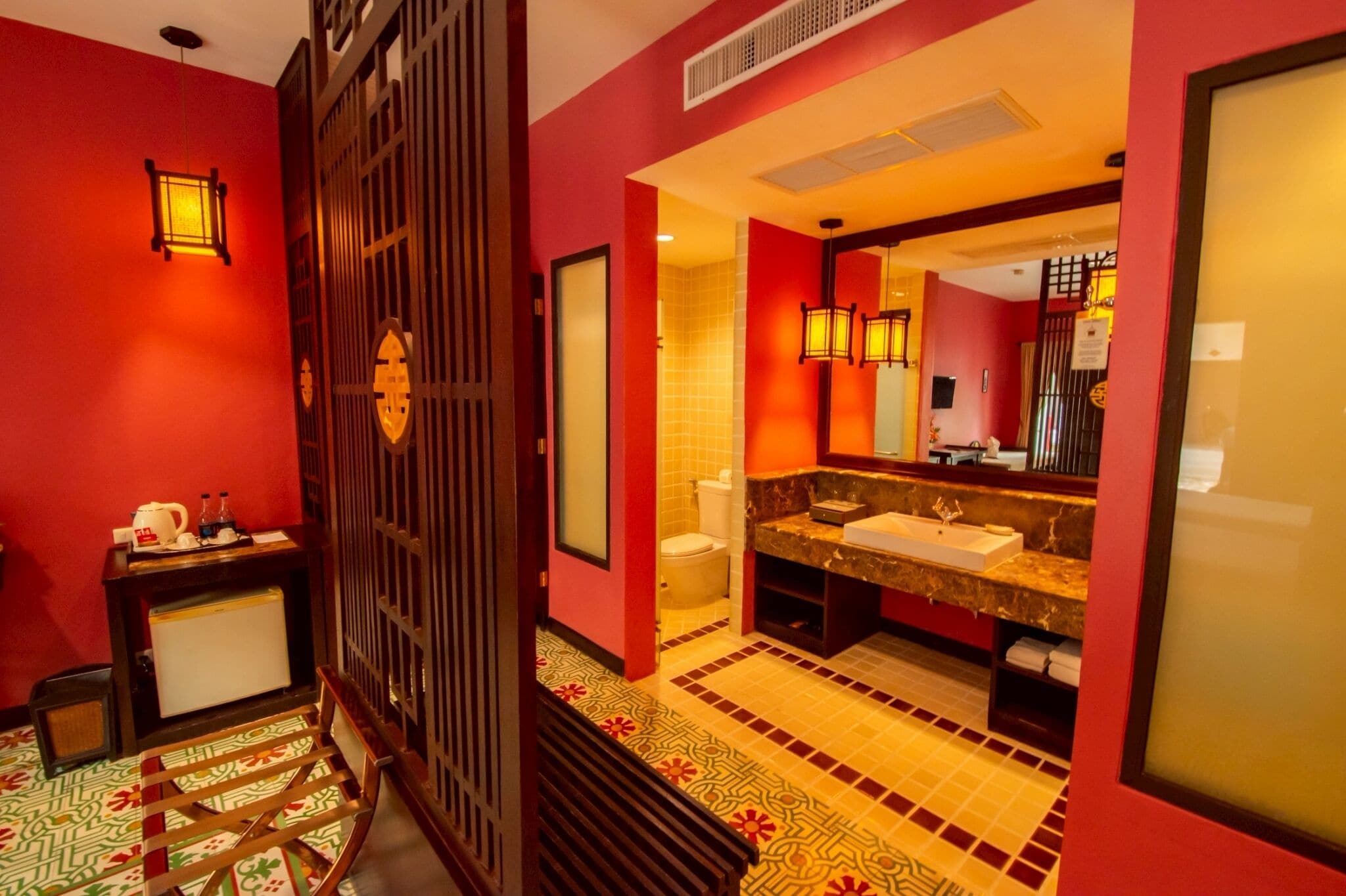 A hotel bathroom with a red and yellow color scheme, a large mirror, a sink, and a toilet.