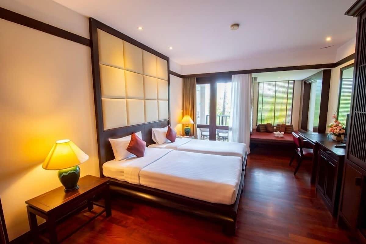A hotel room with two beds, a desk, and a balcony.