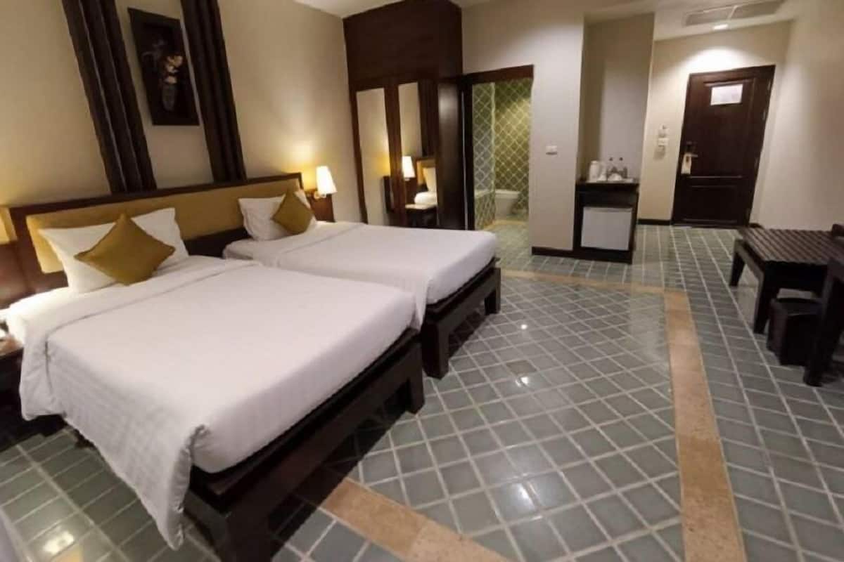 A hotel room with two beds, a small desk, and a bathroom visible through an open door.
