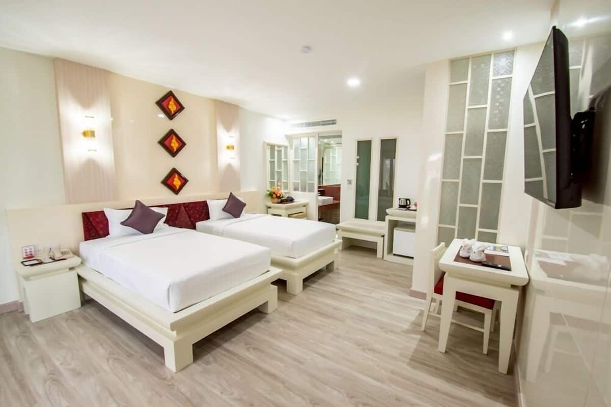 A hotel room with two beds, a desk, a chair, a TV, and a bathroom visible through a glass door.