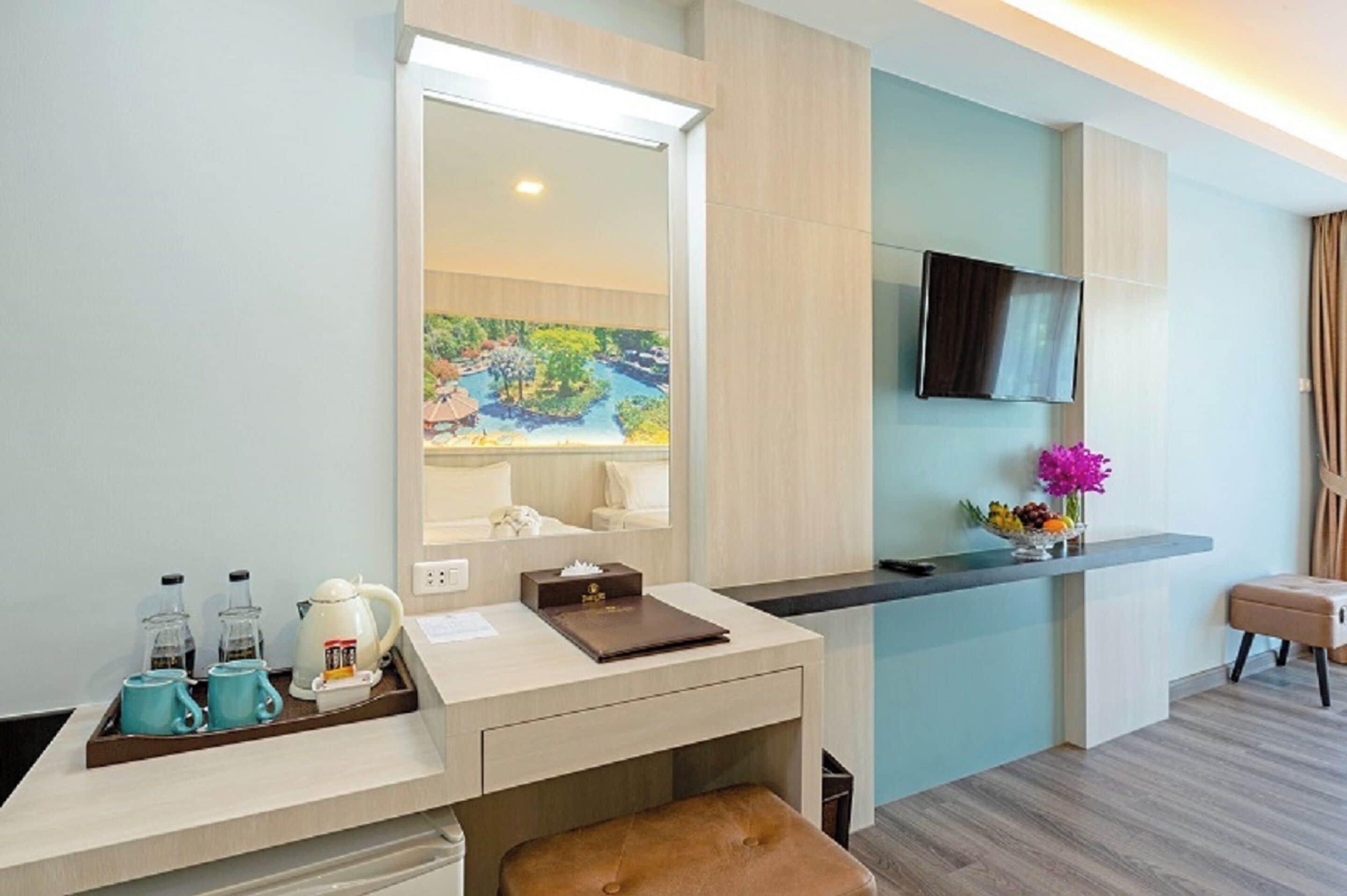 Habitación de hotel con escritorio, un espejo grande, televisor y un cuadro de un paisaje.