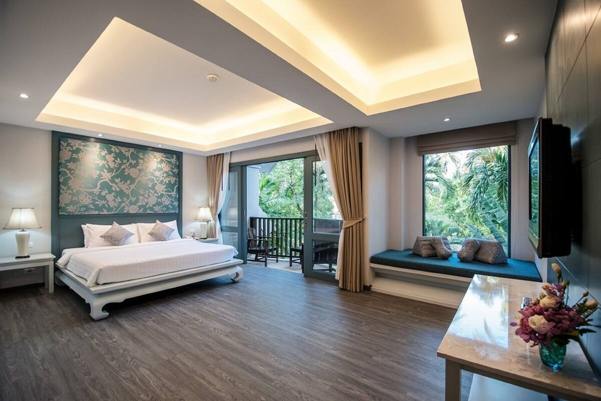 A modern bedroom with a large bed, a seating area by the window, and a TV mounted on the wall.