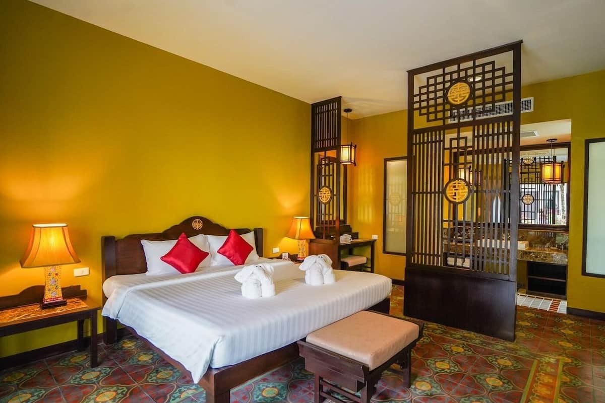 A hotel room with a bed, two bedside tables, a bench, a decorative screen, and a tiled floor.