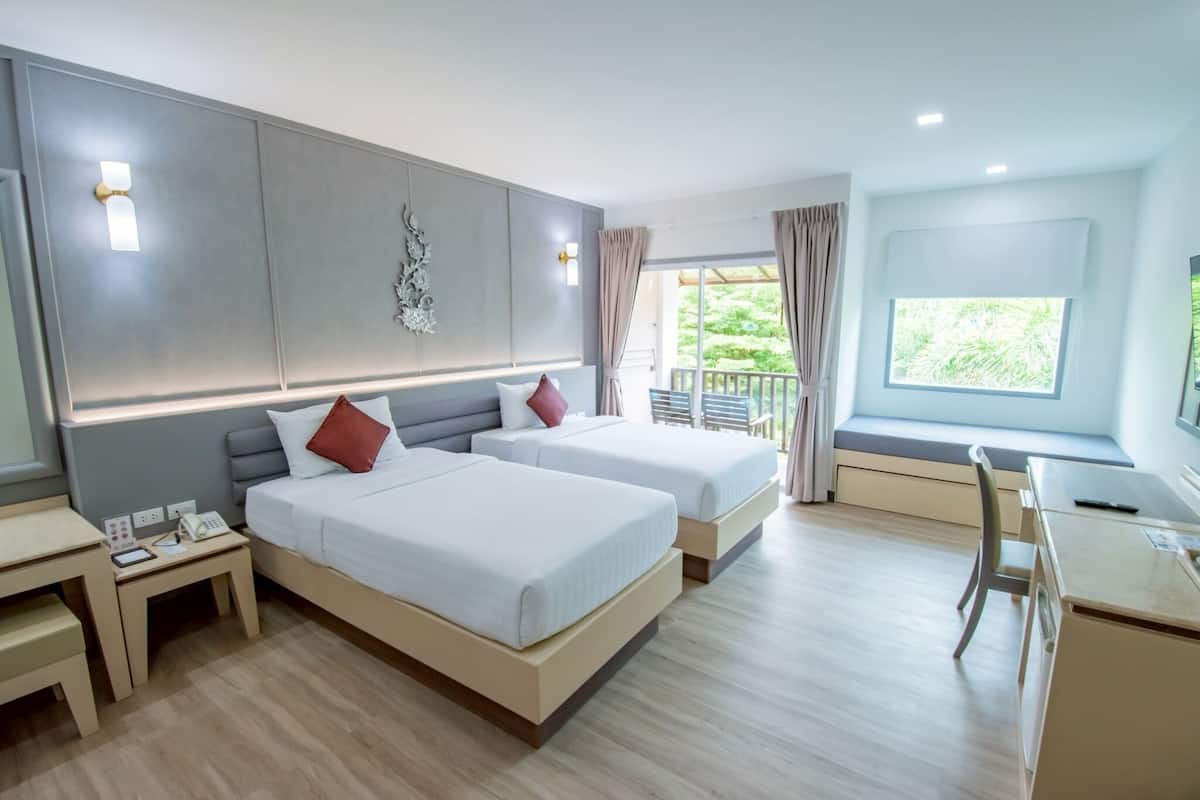 A hotel room with two beds, a desk, a chair, a small table, a phone, and a window with curtains.