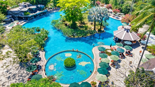 A large outdoor swimming pool surrounded by lush greenery and palm trees, with lounge areas and umbrellas. - Duangjitt Resort, Phuket (Patong)