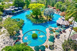 Una gran piscina al aire libre rodeada de exuberante vegetación y palmeras, con zonas de descanso y sombrillas.