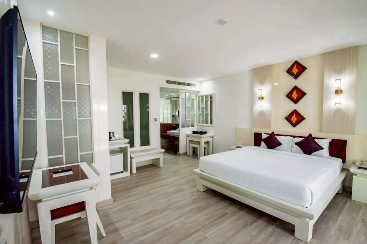 A hotel room with a large bed, a desk, a chair, and a mirror.