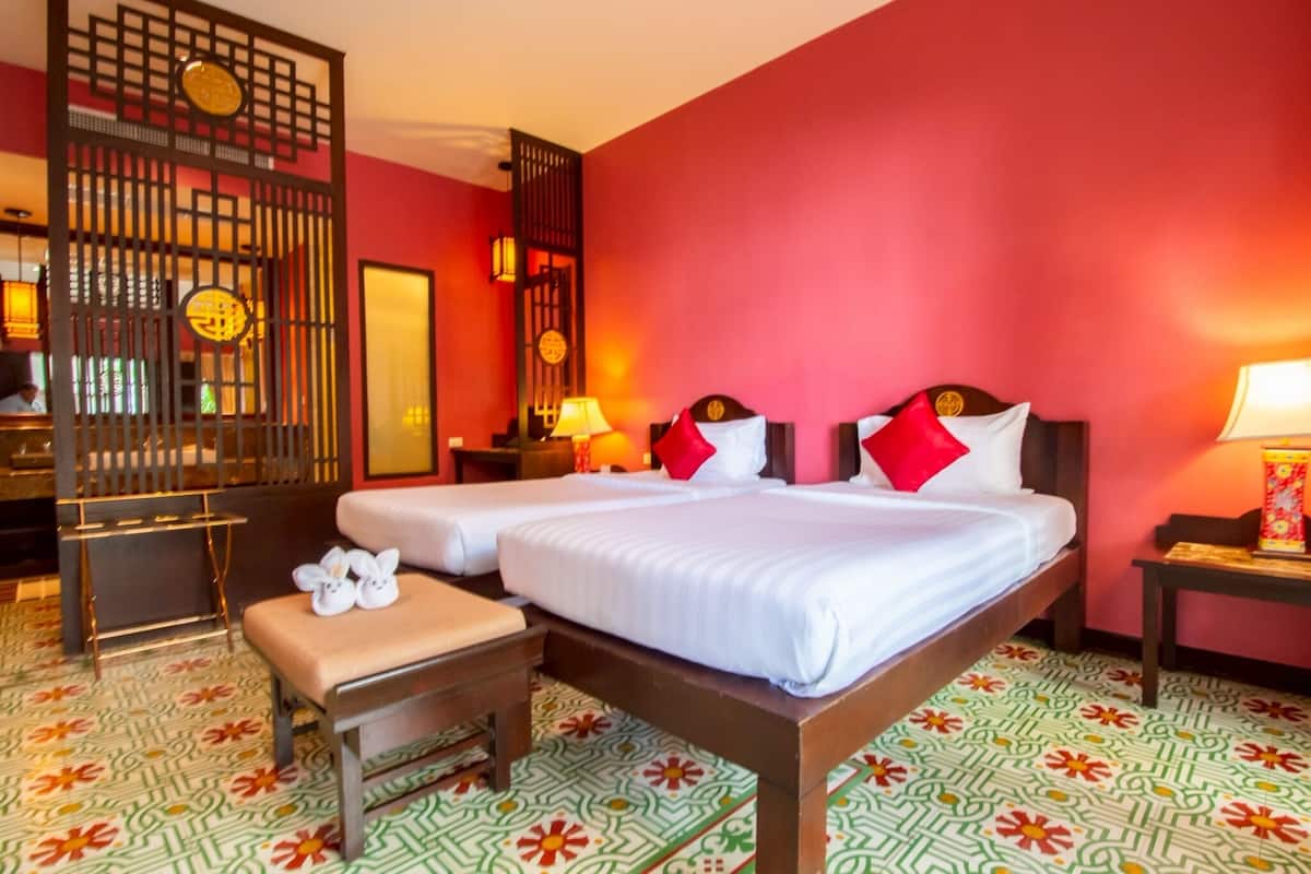 A hotel room with two beds, a wooden bench, a decorative screen, and a patterned floor.