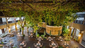 An indoor courtyard with tables and chairs arranged for dining, surrounded by lush greenery and a brick structure. - Duangjitt Resort, Phuket (Patong)