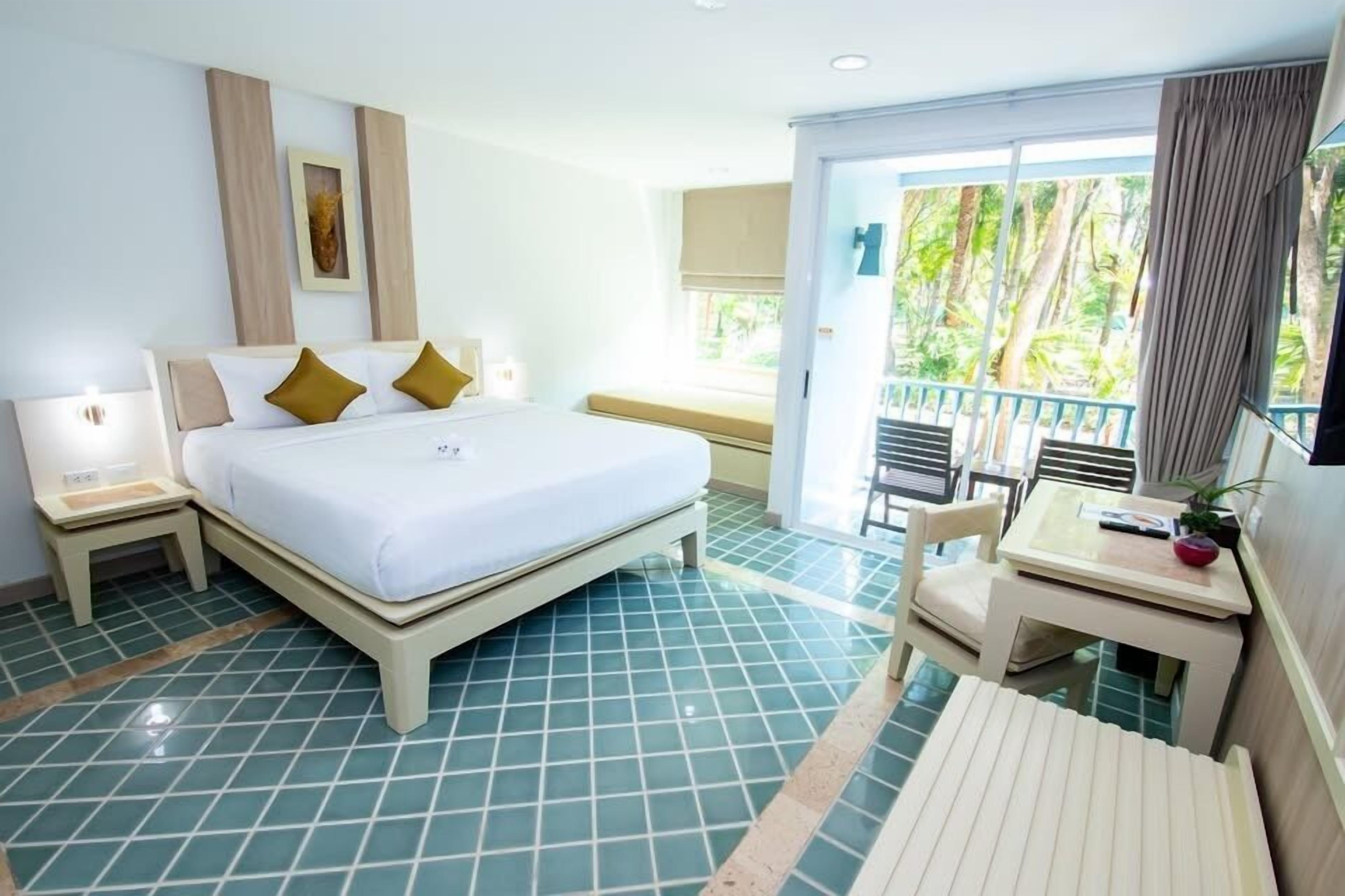 A hotel room with a bed, bedside tables, a small desk, and a balcony with a view of trees.