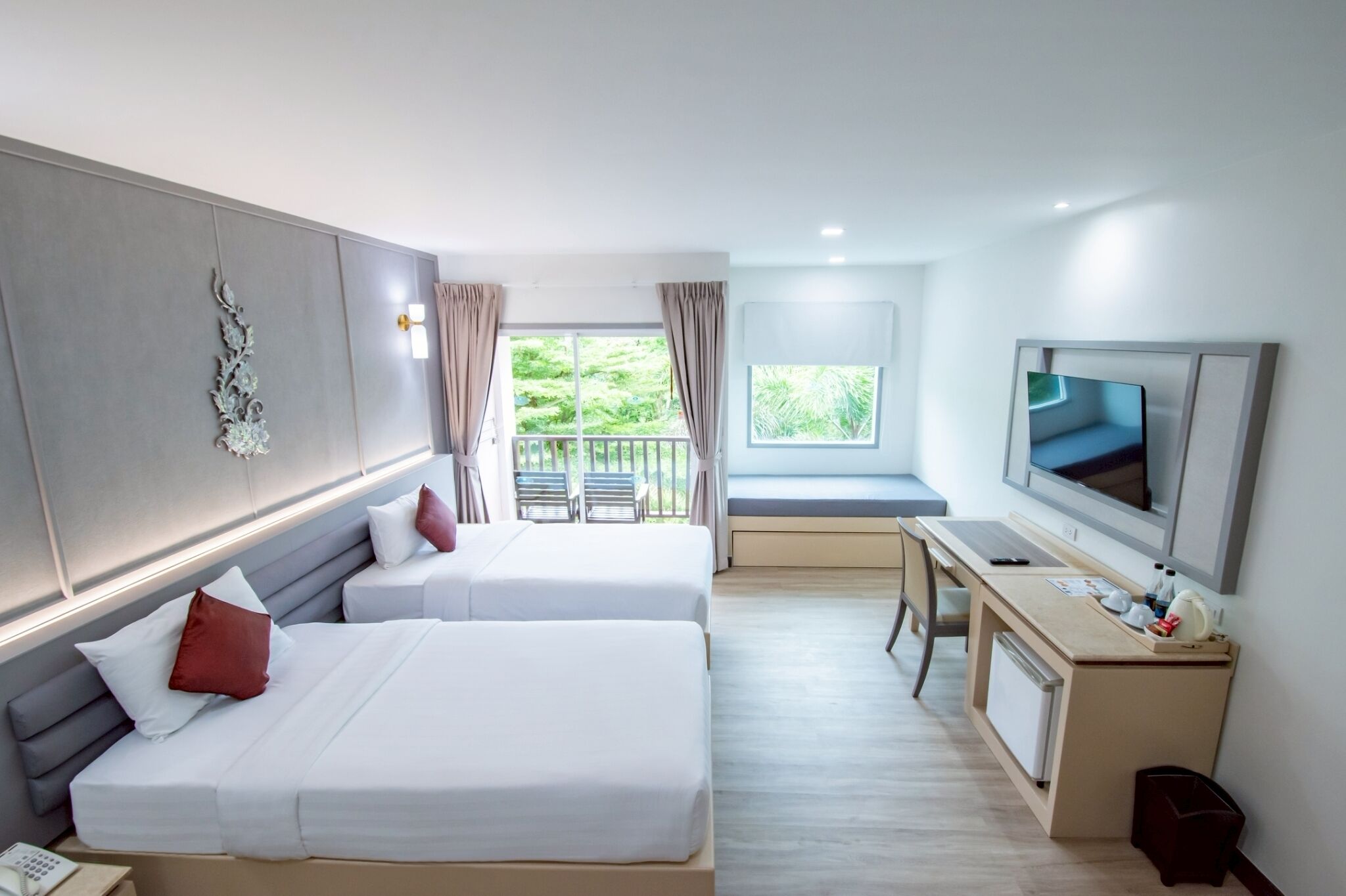 Habitación de hotel con dos camas, un escritorio, un televisor y un balcón con vista a zonas verdes.