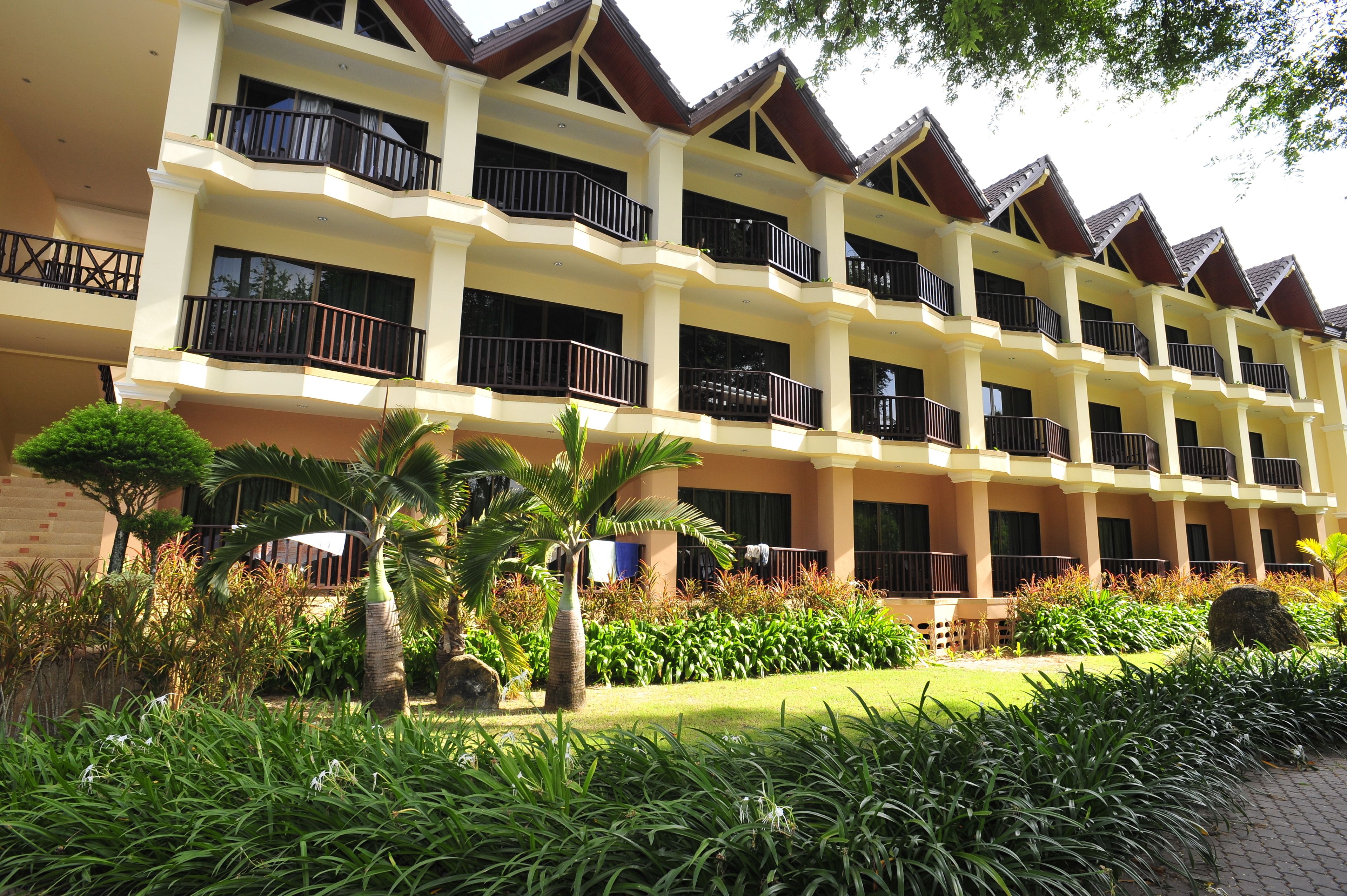 A multi-story hotel with balconies, a well-maintained garden, and a brick facade.