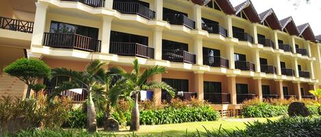 A multi-story hotel with balconies, a well-maintained garden, and a brick facade.