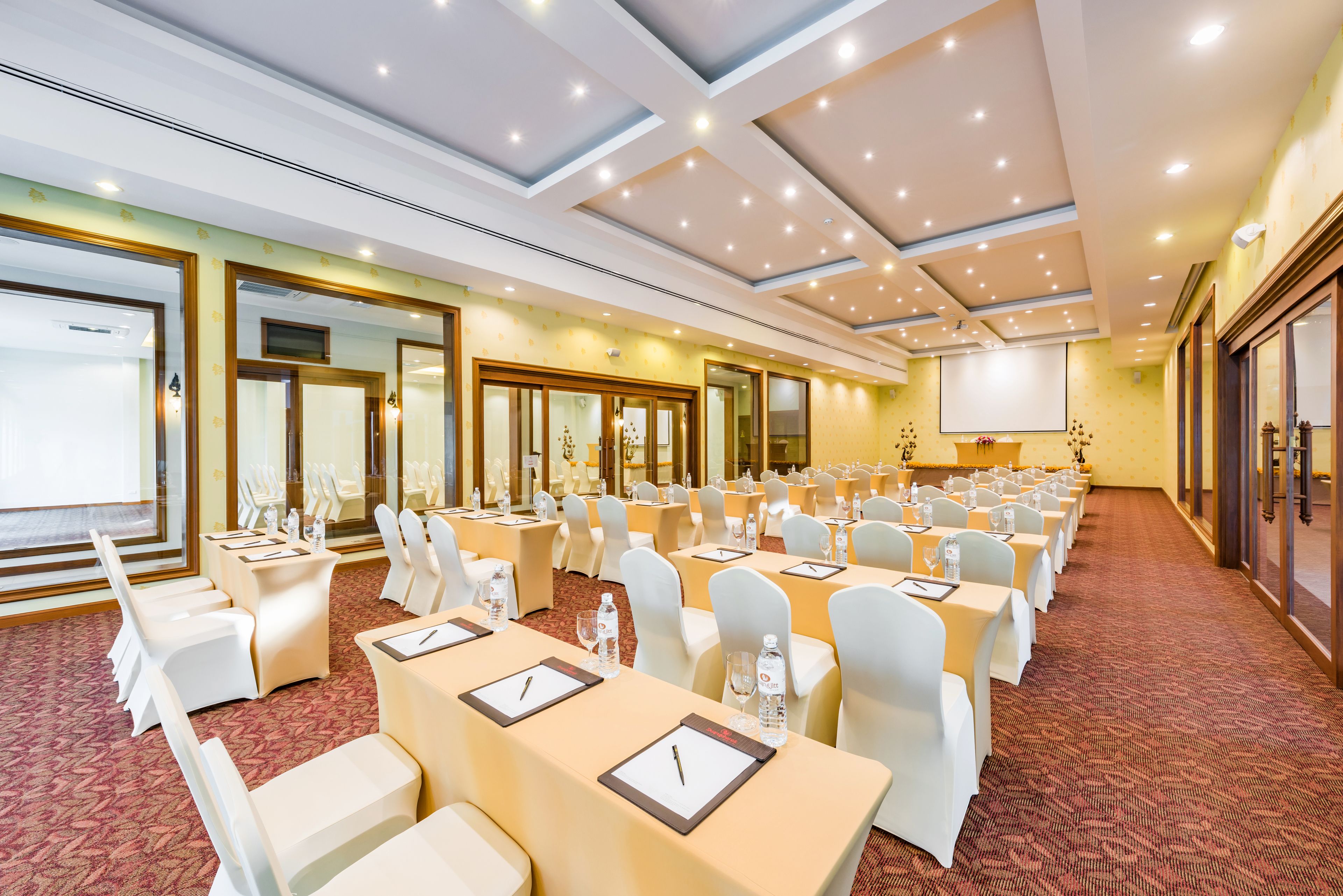 A conference room with rows of tables, chairs, and a large screen.