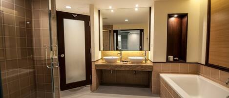 A modern bathroom with a glass shower enclosure, two sinks, a large bathtub, and a mirror above the sinks.