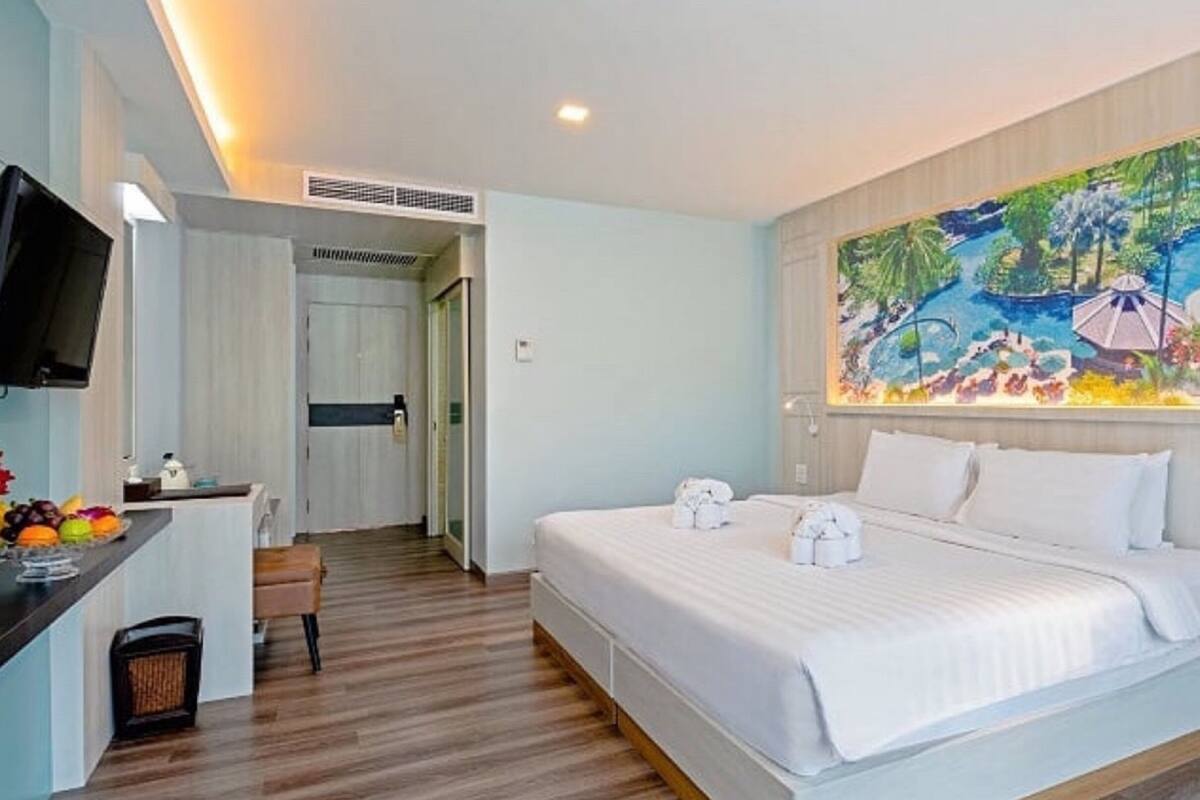 A hotel room with a large bed, a desk with a flat-screen TV, a painting on the wall, and a bathroom visible through an open door.