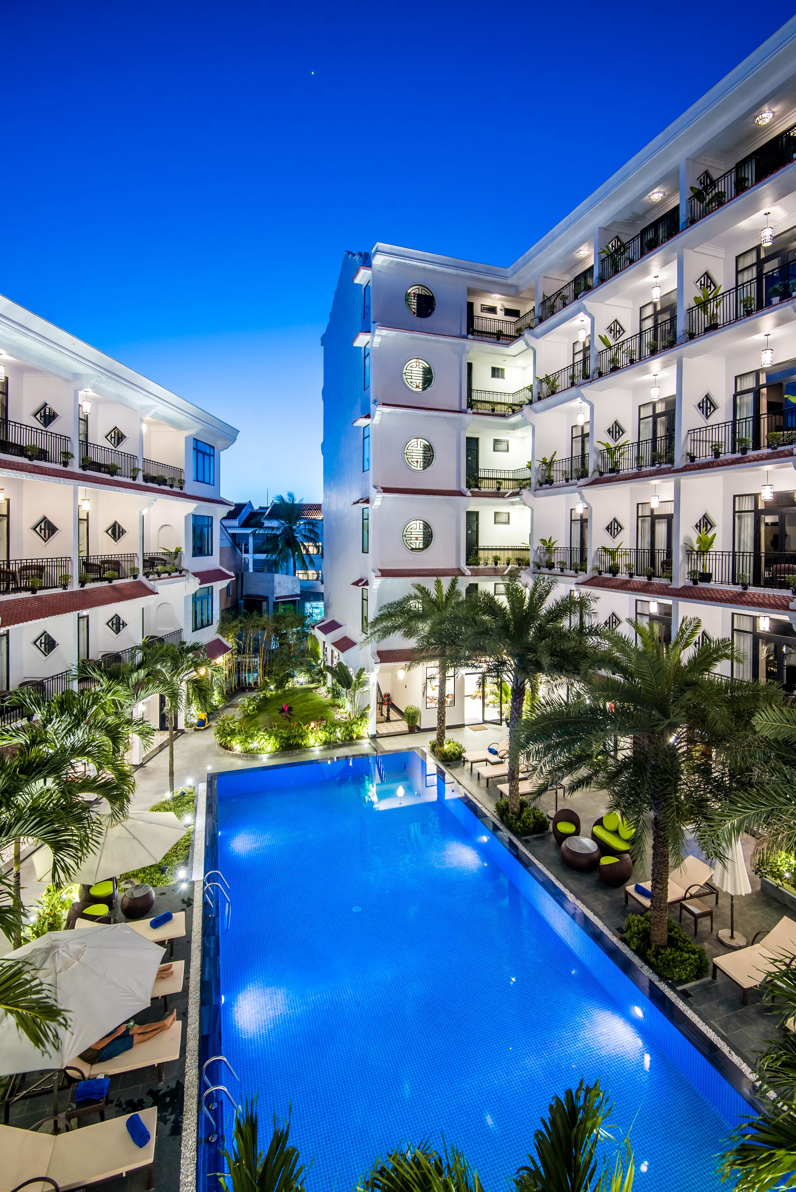 Un hotel con varios balcones, piscina y abundante vegetación.
